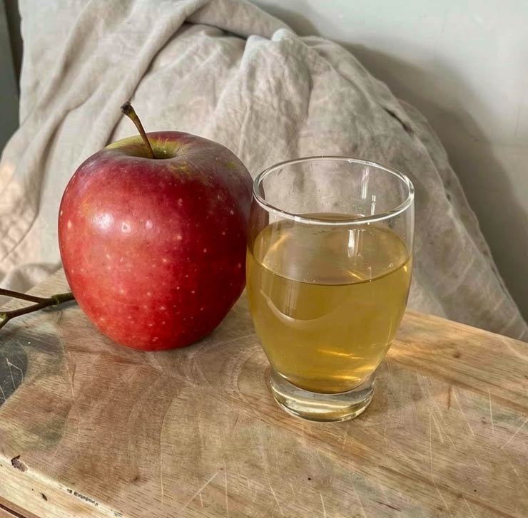 A whole apple beside a glass of apple juice